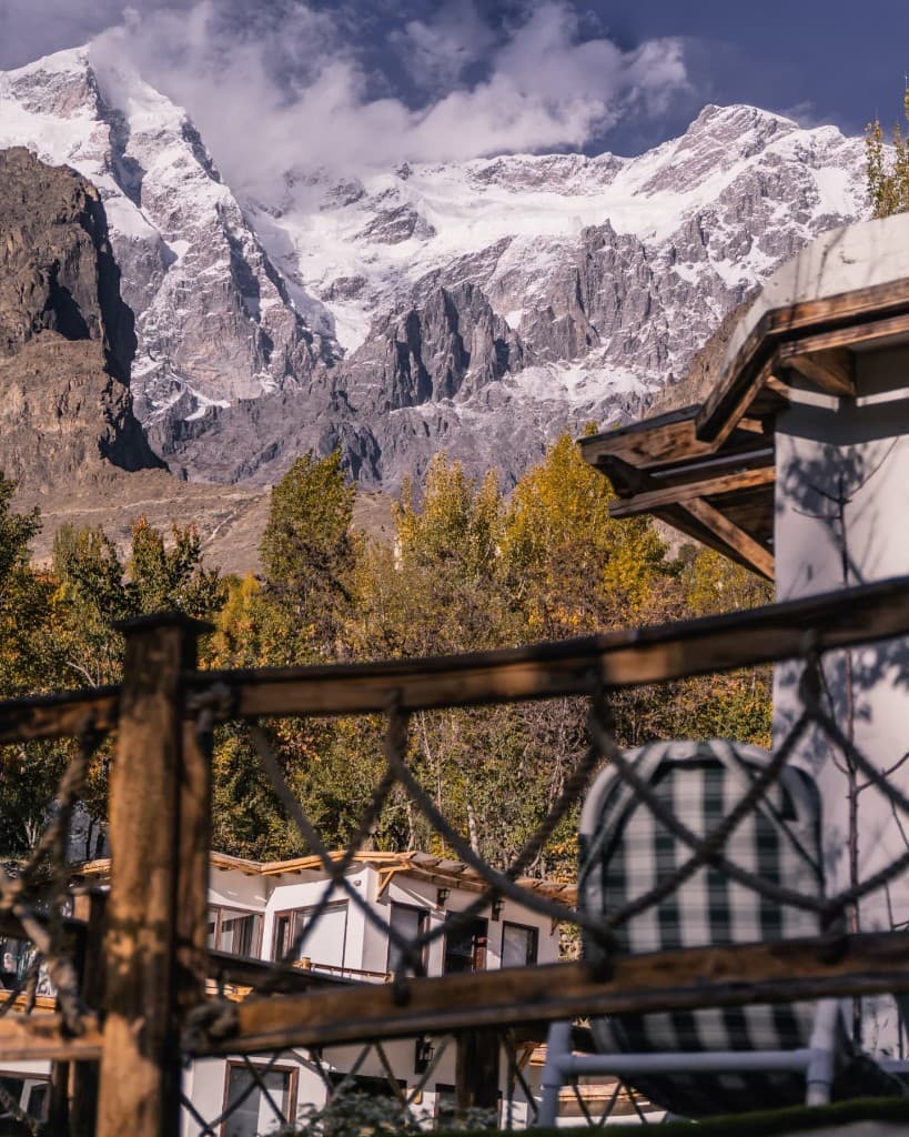 Snow-capped Hunza peaks above autumn trees, seen from Offsite Offto's rope-rail wooden terrace